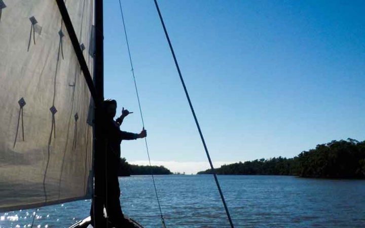 a person gives a hang loose sign while holding a rope on a sailboat on an outward bound expedition